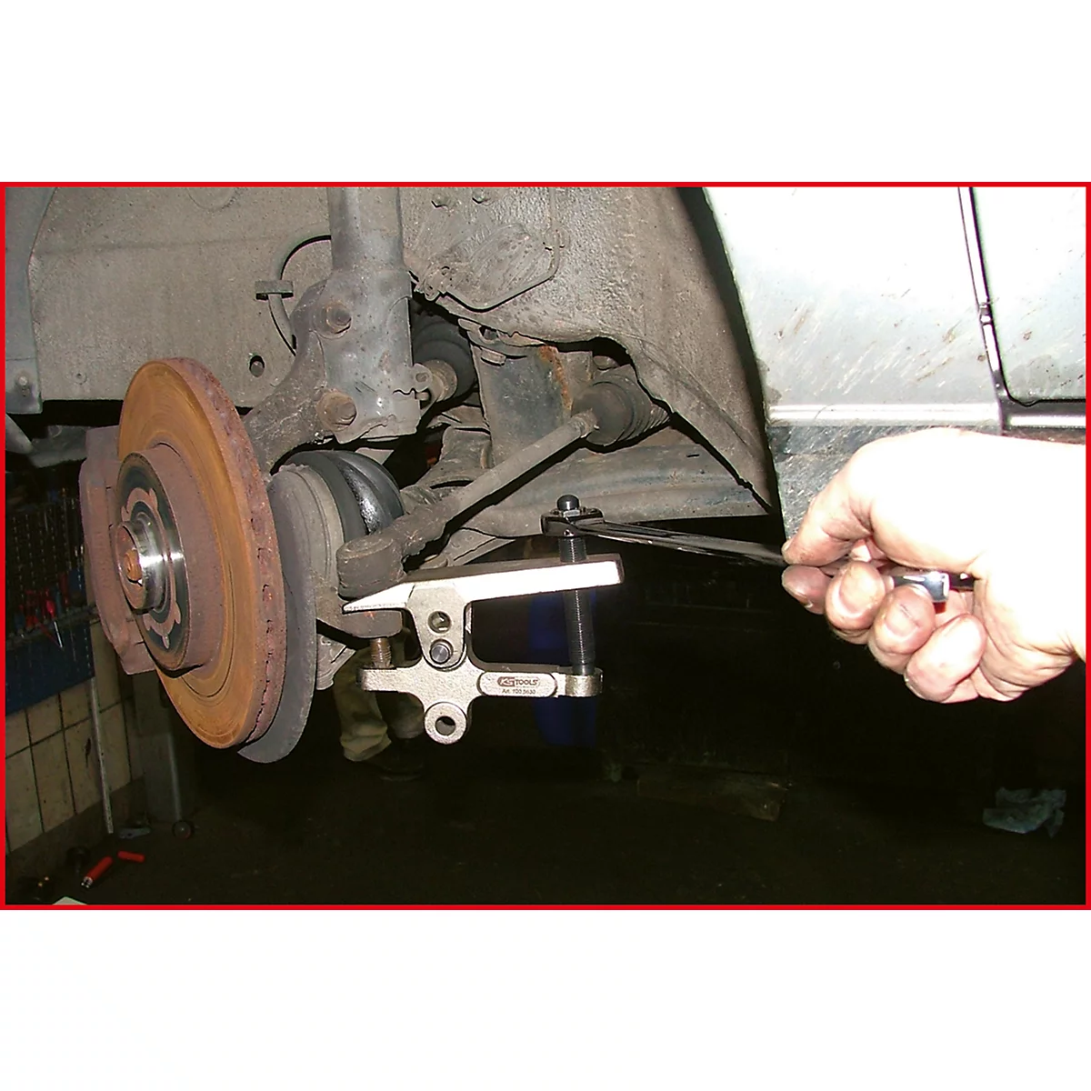 Nahaufnahme eines Autos: Ein Mechaniker arbeitet an der Bremsscheibe und verwendet ein Spezialwerkzeug, um die Bremszange zu manipulieren.